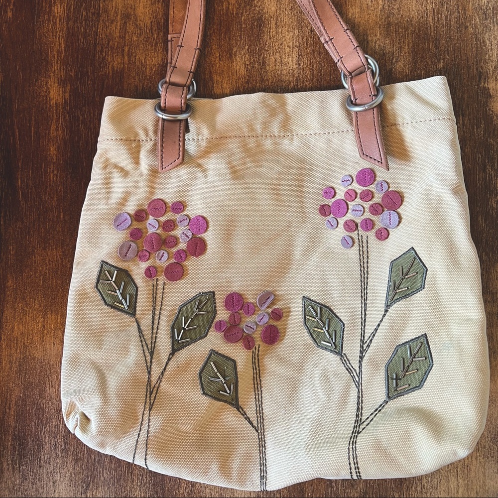 Canvas Fossil tote with embroidered/sewn flower pattern and clean plum interior.